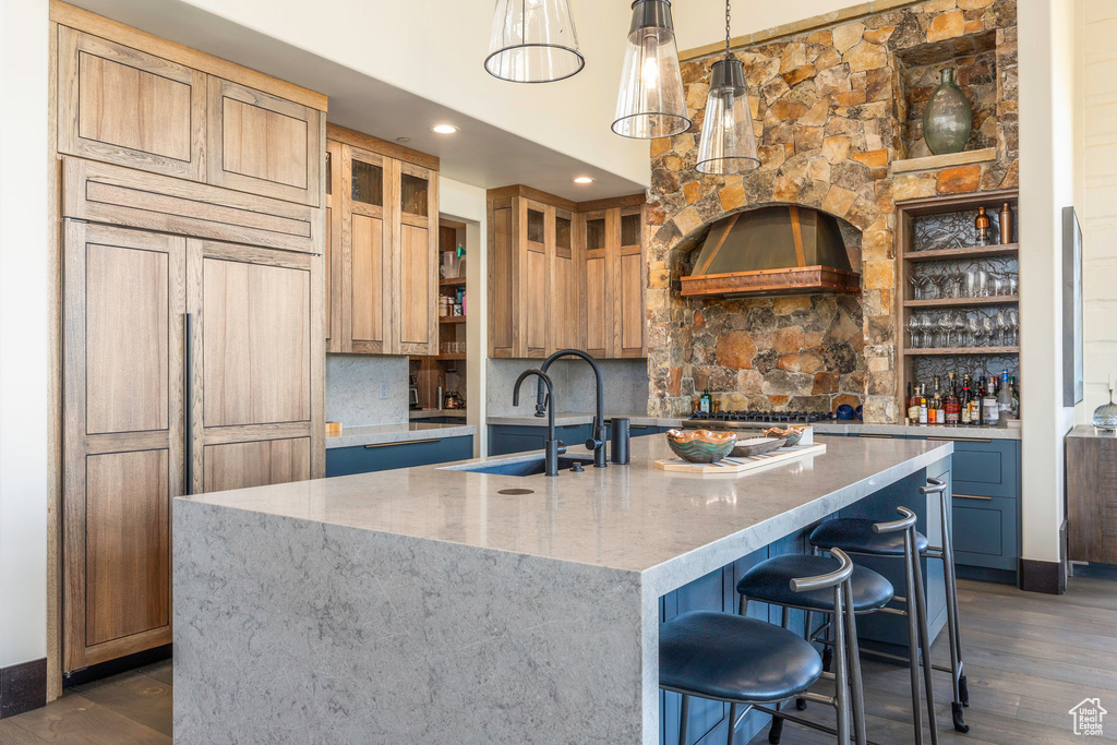 Kitchen with pendant lighting, backsplash, sink, an island with sink, and light stone counters