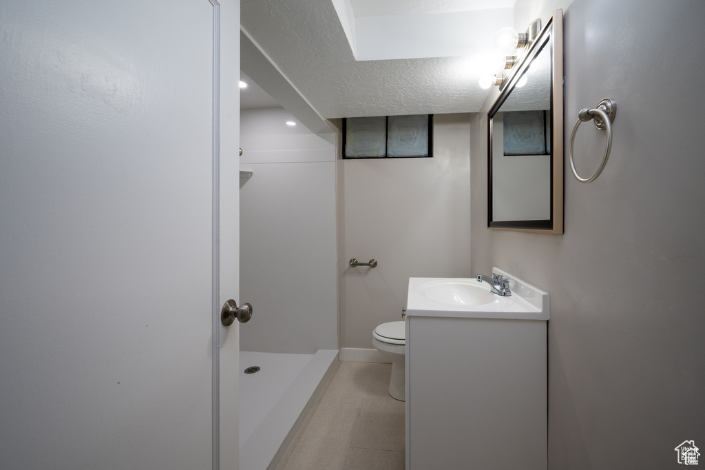 Bathroom featuring walk in shower, vanity, a textured ceiling, and toilet