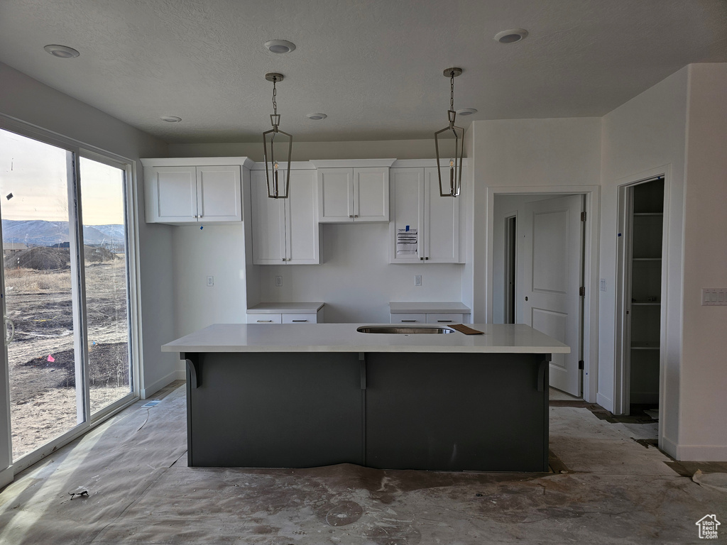 Kitchen with a mountain view, pendant lighting, white cabinets, and an island with sink
