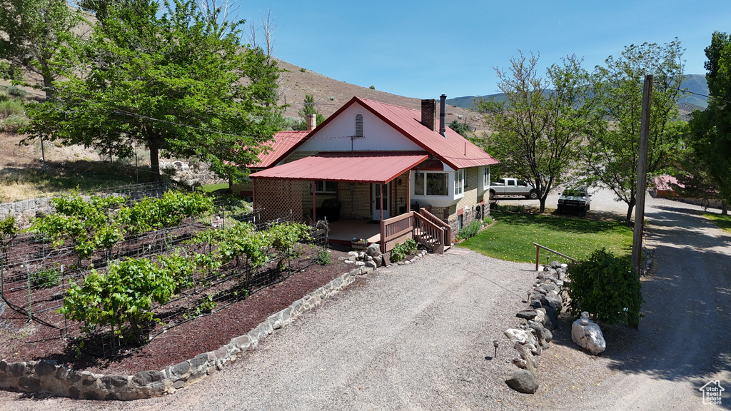 View of front facade featuring a chimney, a garden, a mountain view, metal roof, and gravel driveway