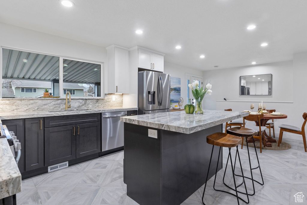 Kitchen with a center island, sink, stainless steel appliances, light parquet flooring, and white cabinets