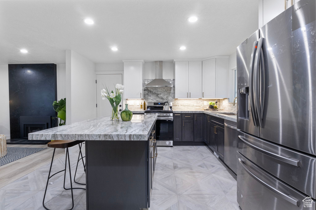 Kitchen with appliances with stainless steel finishes, wall chimney exhaust hood, a breakfast bar, a center island, and white cabinetry