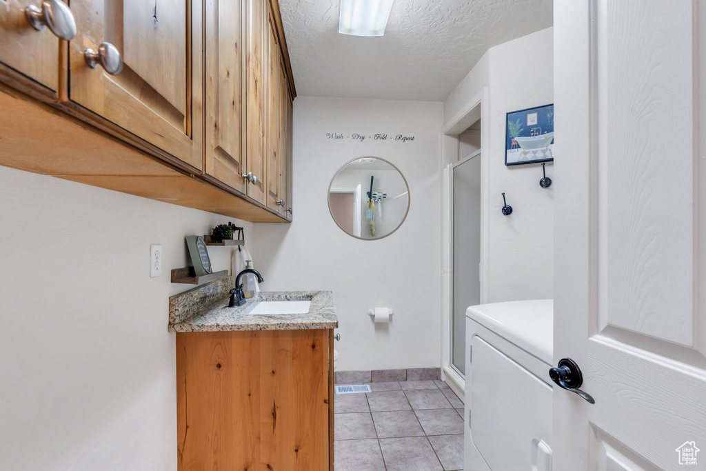 Bathroom with a textured ceiling, vanity, a shower with door, tile patterned flooring, and washer / dryer