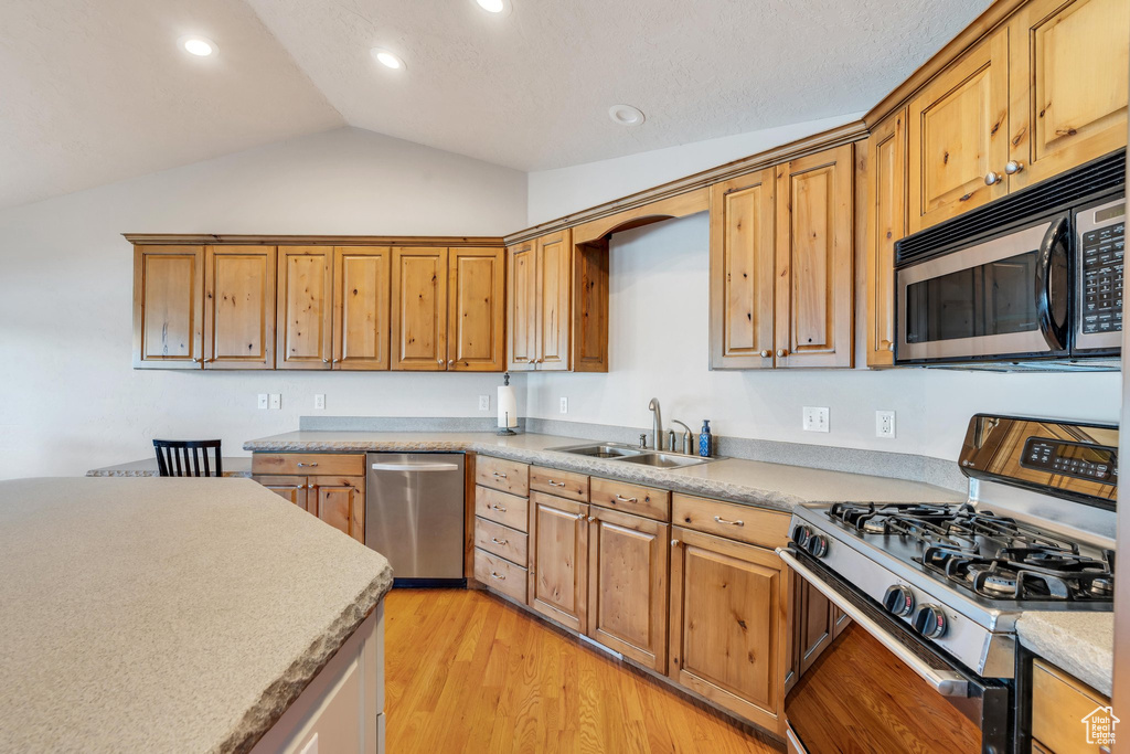 Kitchen featuring light wood-type flooring, sink, appliances with stainless steel finishes, and vaulted ceiling