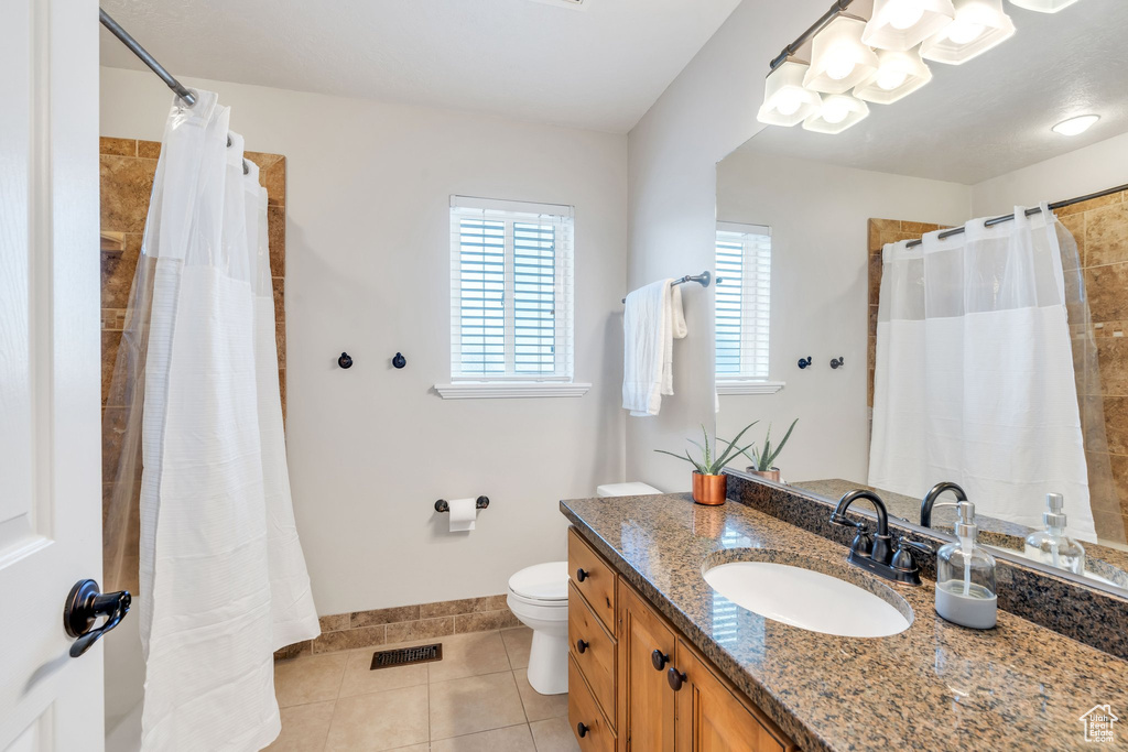 Bathroom with tile patterned floors, curtained shower, vanity, and toilet