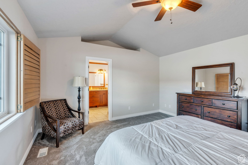 Bedroom featuring ceiling fan, vaulted ceiling, light carpet, and ensuite bath