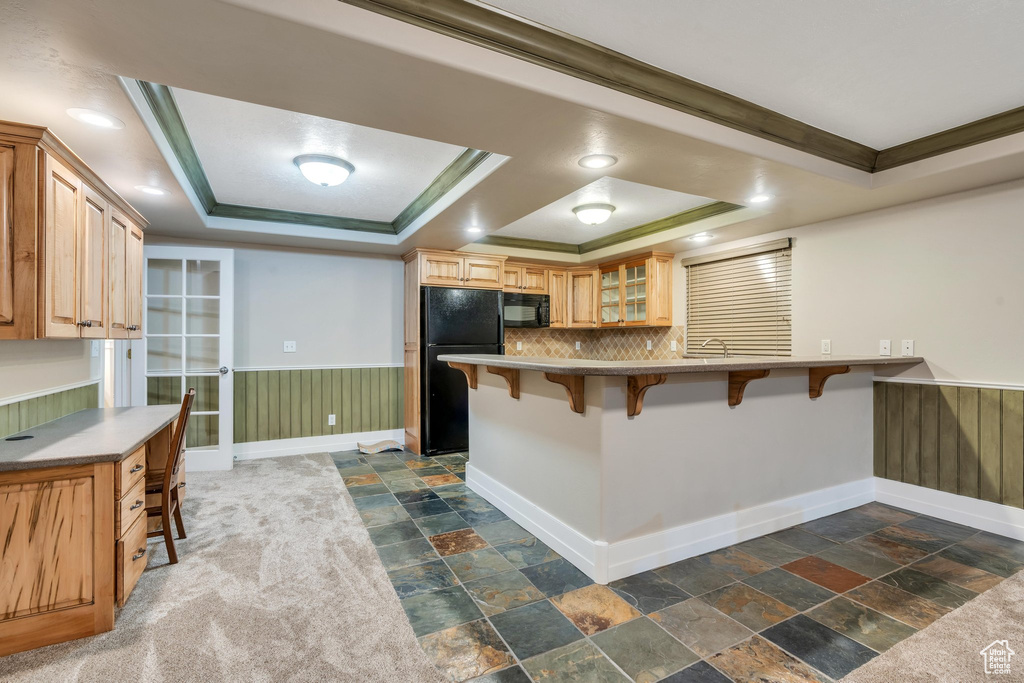 Kitchen featuring a breakfast bar, black appliances, crown molding, a tray ceiling, and kitchen peninsula