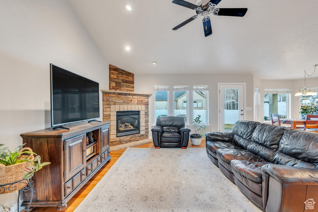 Living room with a stone fireplace, a healthy amount of sunlight, ceiling fan with notable chandelier, and light hardwood / wood-style floors