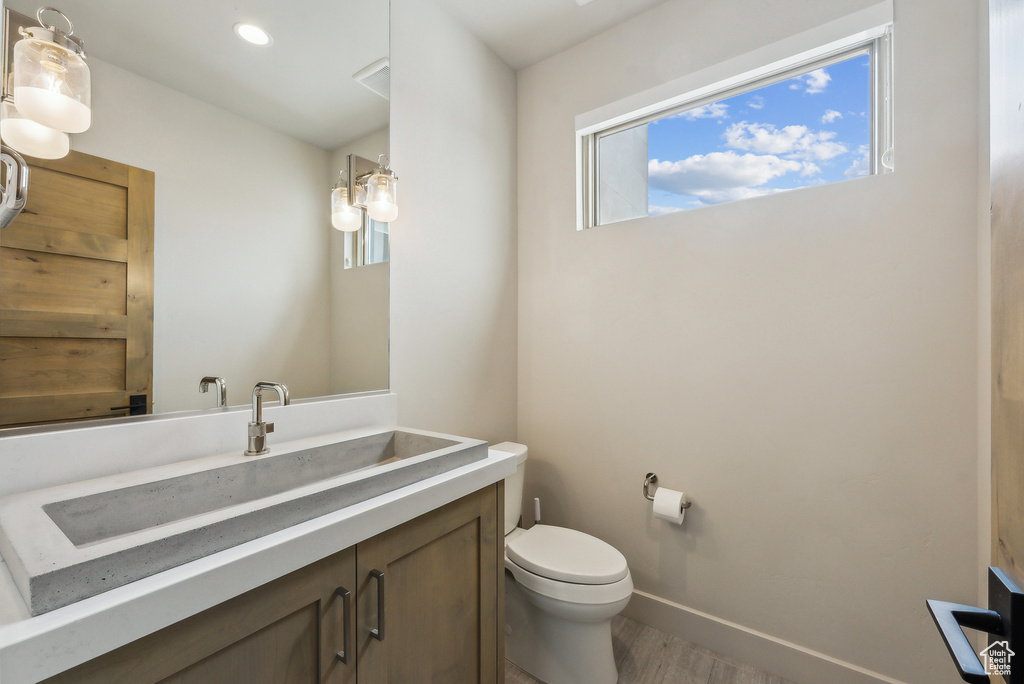 Bathroom featuring toilet, wood finished floors, vanity, baseboards, and recessed lighting