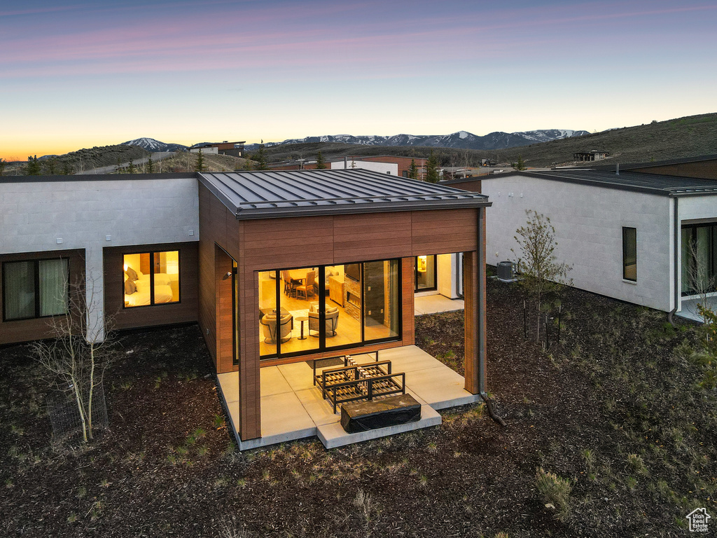 Back of house at dusk with a standing seam roof, metal roof, a mountain view, and a patio