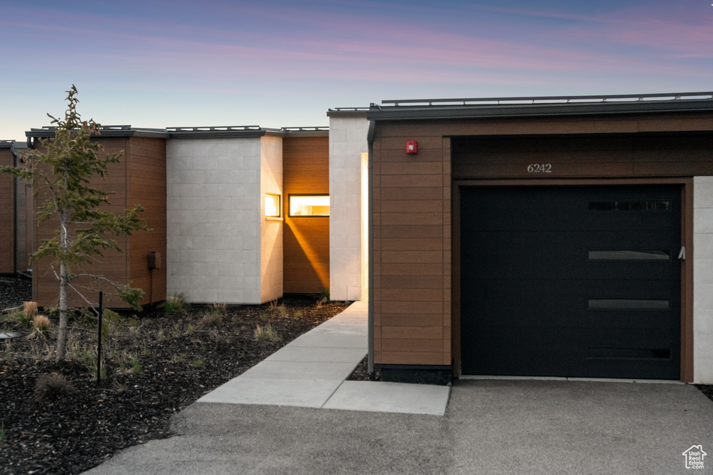 Exterior entry at dusk with concrete block siding, an attached garage, and driveway