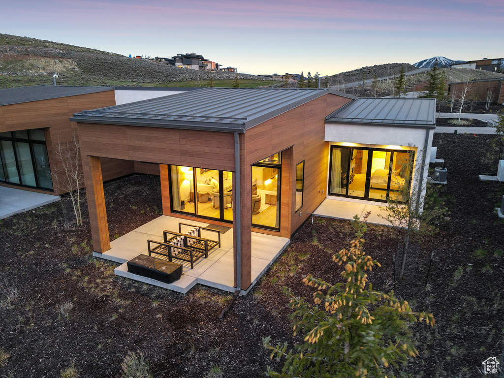 Back of property at dusk with a standing seam roof, a patio, and metal roof