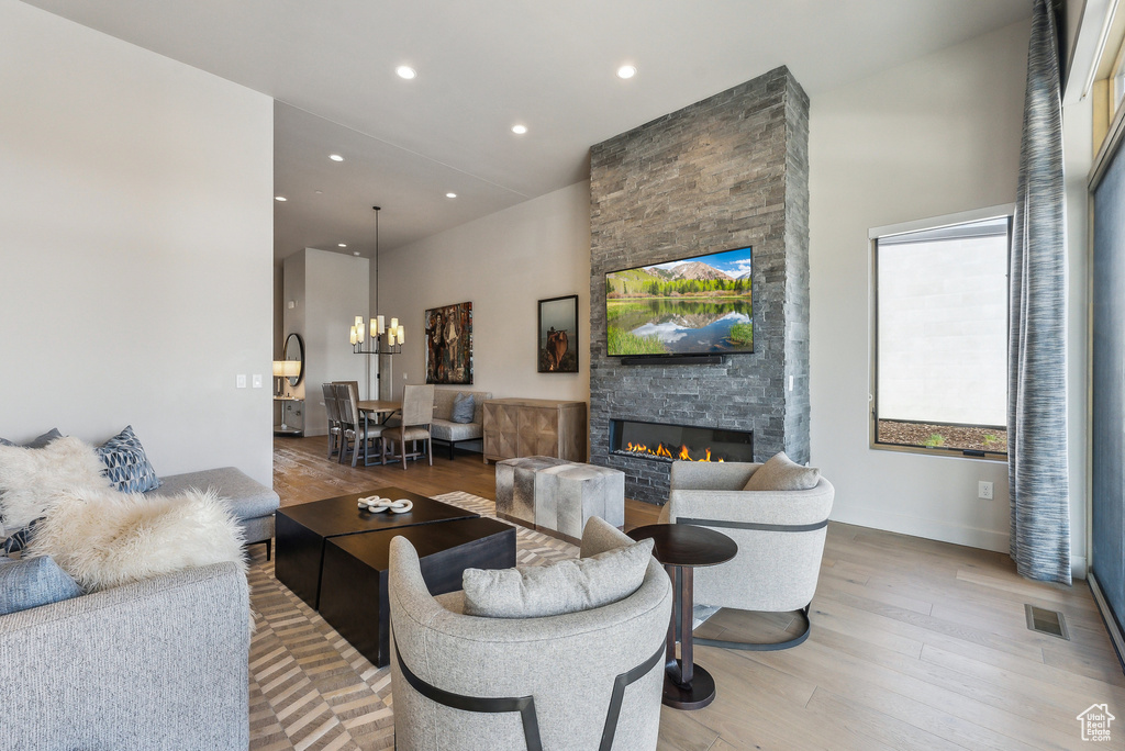 Living room featuring light wood finished floors, a stone fireplace, a chandelier, and recessed lighting