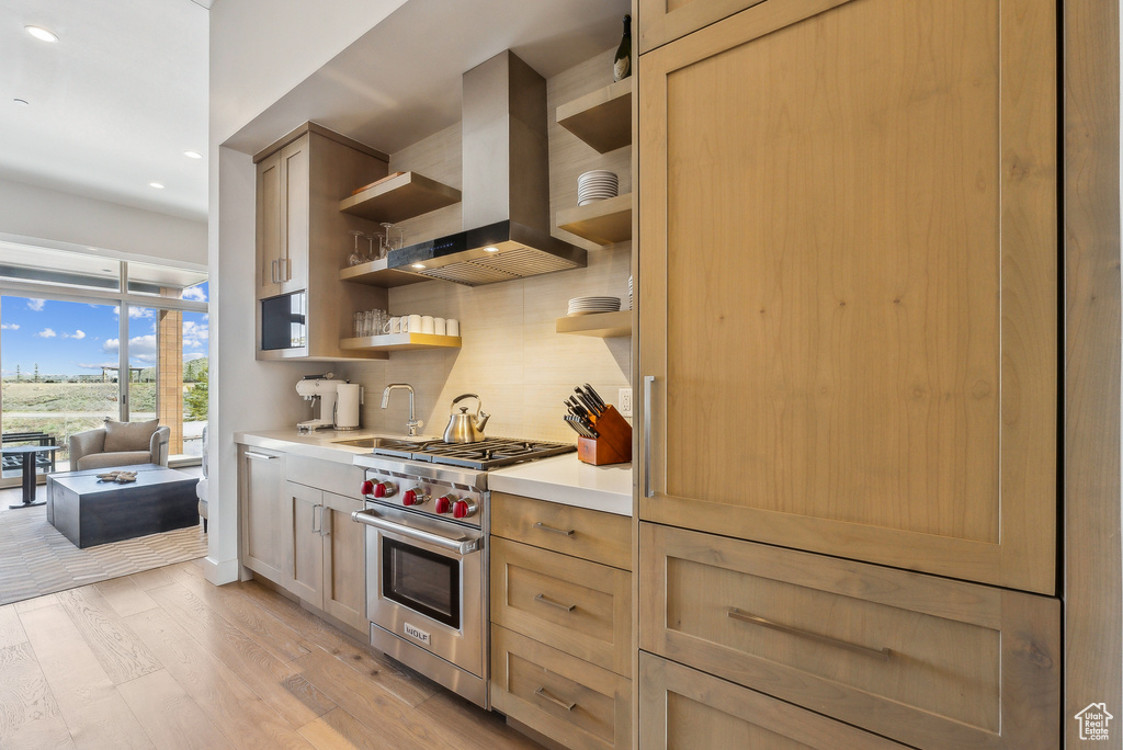 Kitchen with premium range, open shelves, wall chimney range hood, a sink, and light countertops