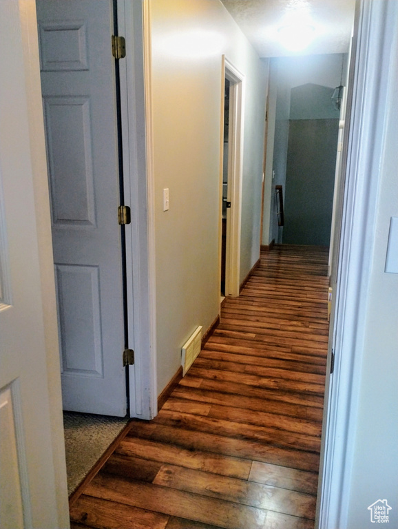 Hall with dark wood-type flooring, baseboards, and visible vents