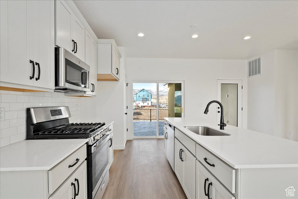 Kitchen with appliances with stainless steel finishes, light wood-type flooring, a kitchen island with sink, sink, and white cabinetry