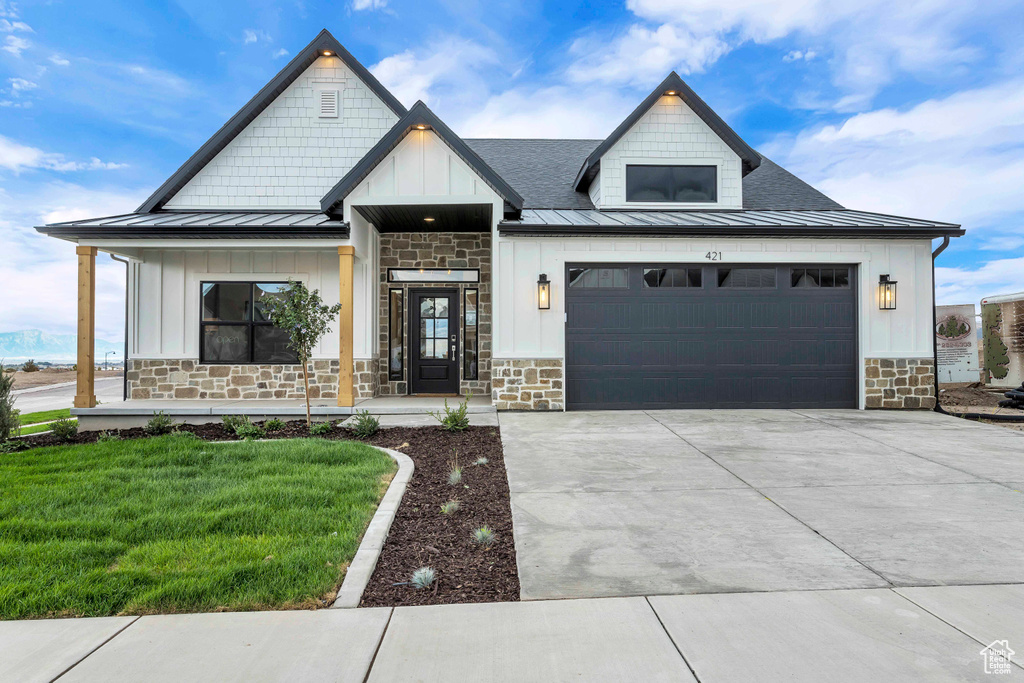 Modern farmhouse with a garage, concrete driveway, stone siding, a standing seam roof, and a front lawn