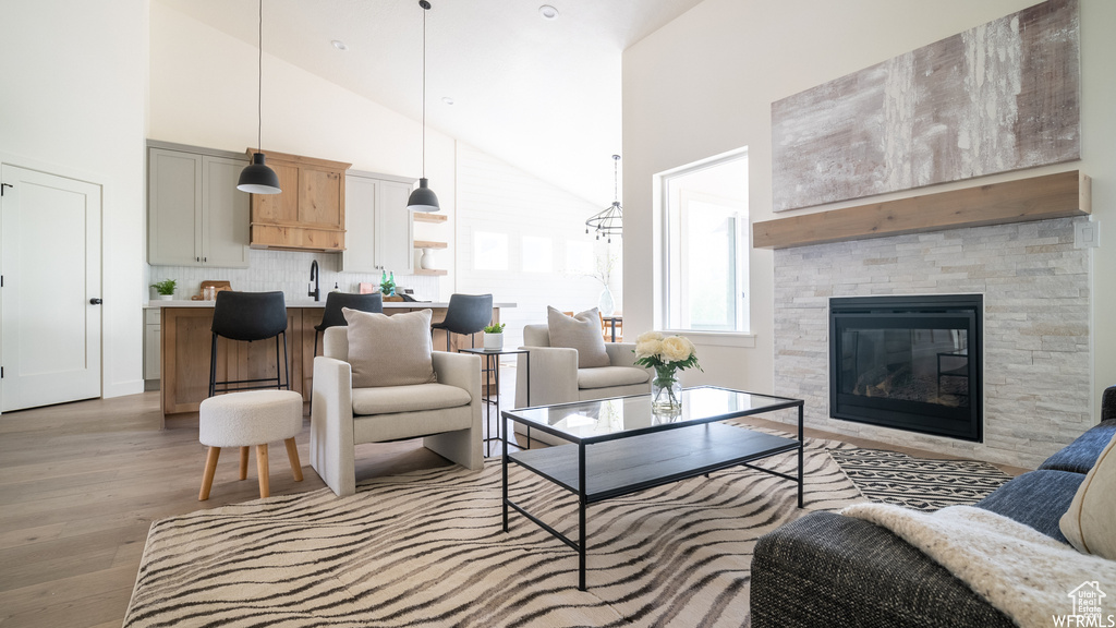 Living room with light hardwood / wood-style floors, a stone fireplace, sink, and high vaulted ceiling