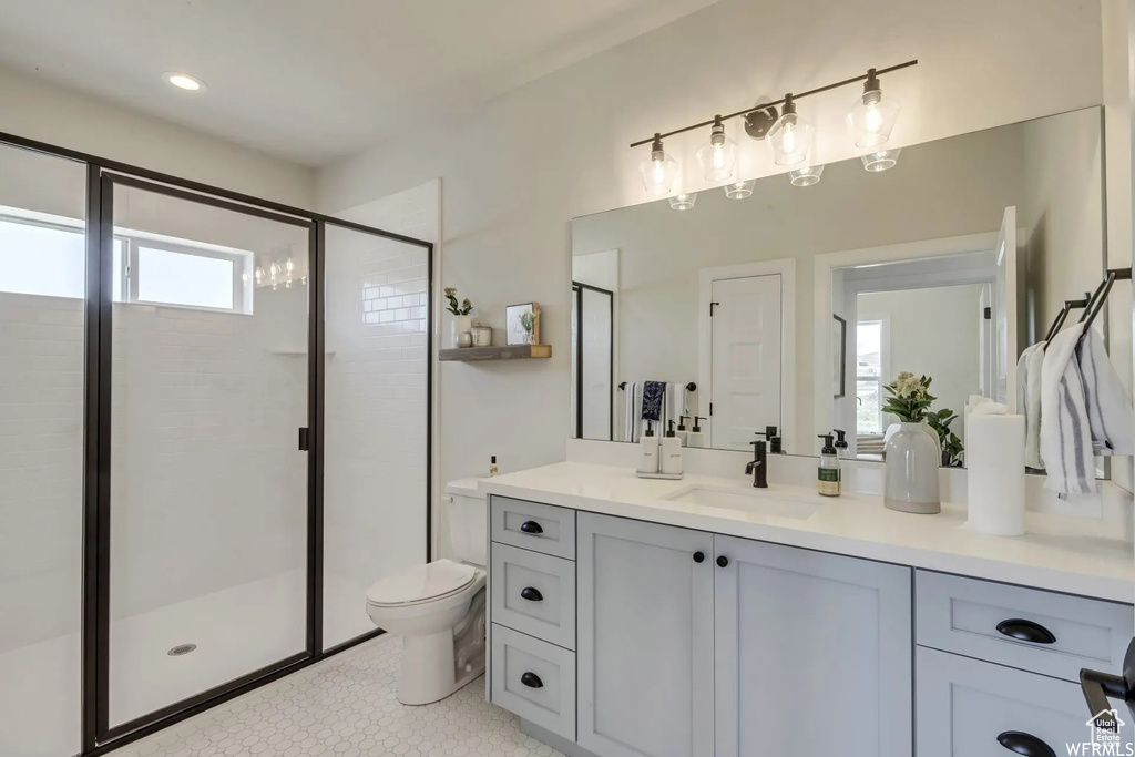 Bathroom featuring tile patterned flooring, vanity, toilet, and a shower with door