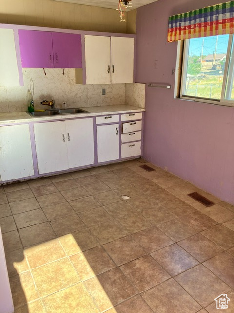 Kitchen with white cabinets, backsplash, light tile patterned floors, and sink