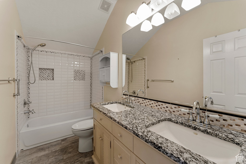 Bathroom featuring lofted ceiling, washtub / shower combination, toilet, wood finished floors, and double vanity