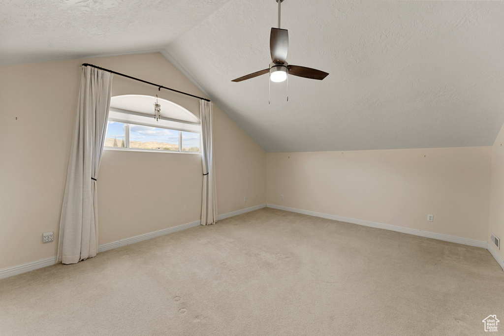 Bonus room featuring a textured ceiling, a ceiling fan, vaulted ceiling, carpet flooring, and baseboards