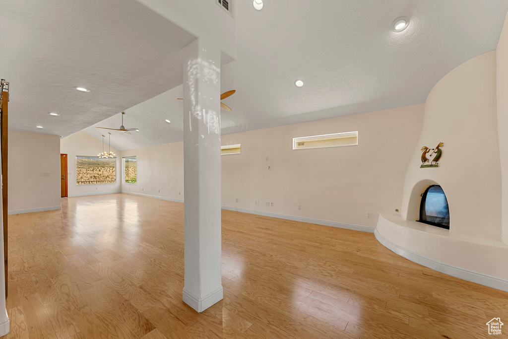 Unfurnished living room featuring lofted ceiling, light wood-style flooring, baseboards, a chandelier, and recessed lighting