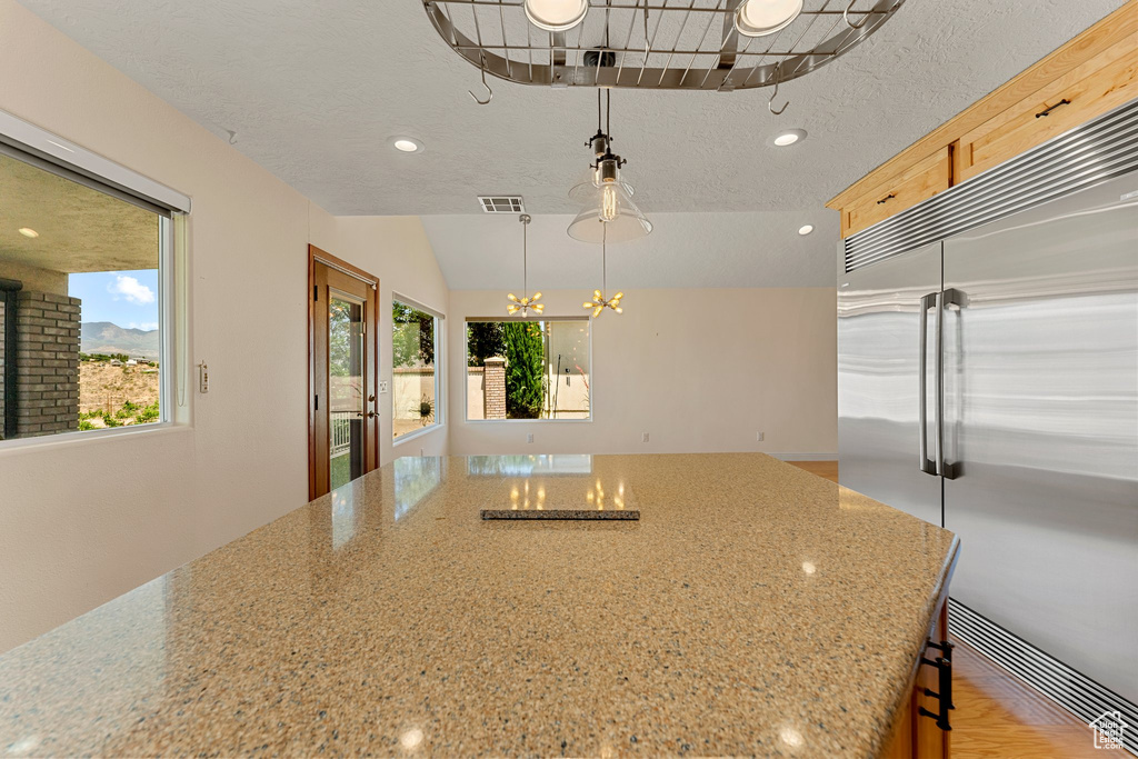 Kitchen featuring stainless steel built in fridge, a chandelier, recessed lighting, light stone countertops, and hanging light fixtures
