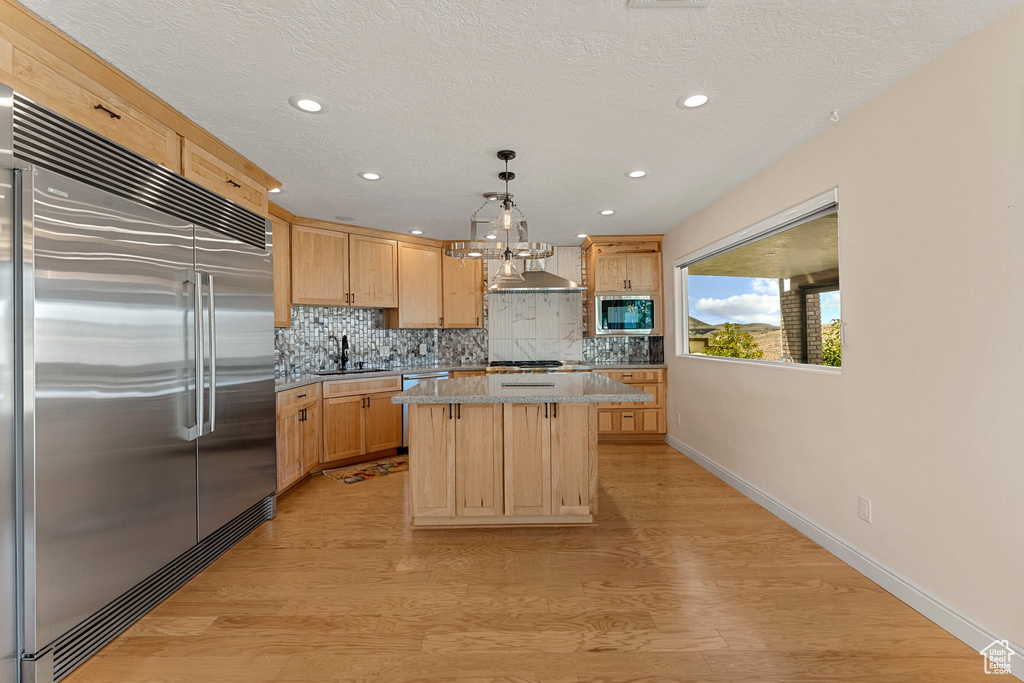 Kitchen featuring built in appliances, light brown cabinetry, decorative backsplash, light wood-type flooring, and recessed lighting