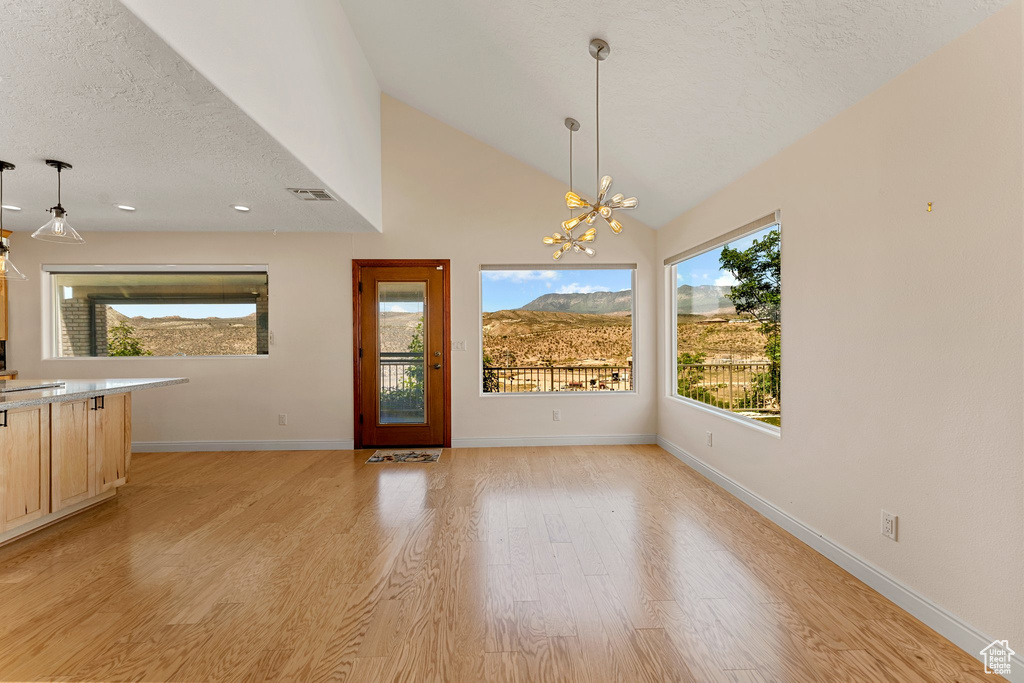 Unfurnished dining area with light wood-style flooring, a chandelier, baseboards, a textured ceiling, and lofted ceiling