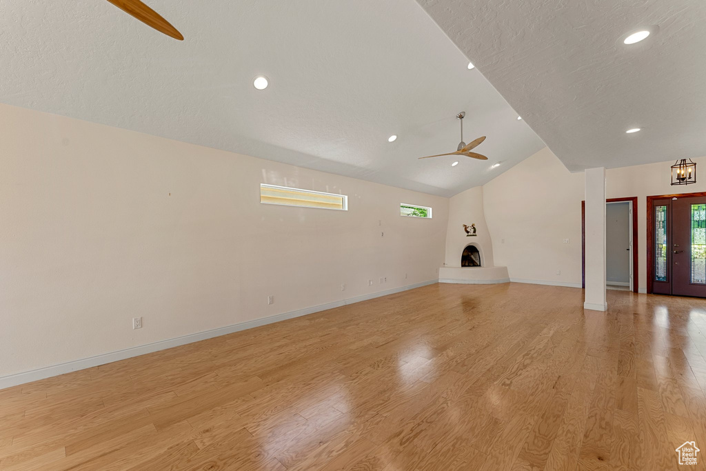 Unfurnished living room featuring a large fireplace, ceiling fan, light wood-style floors, vaulted ceiling, and baseboards