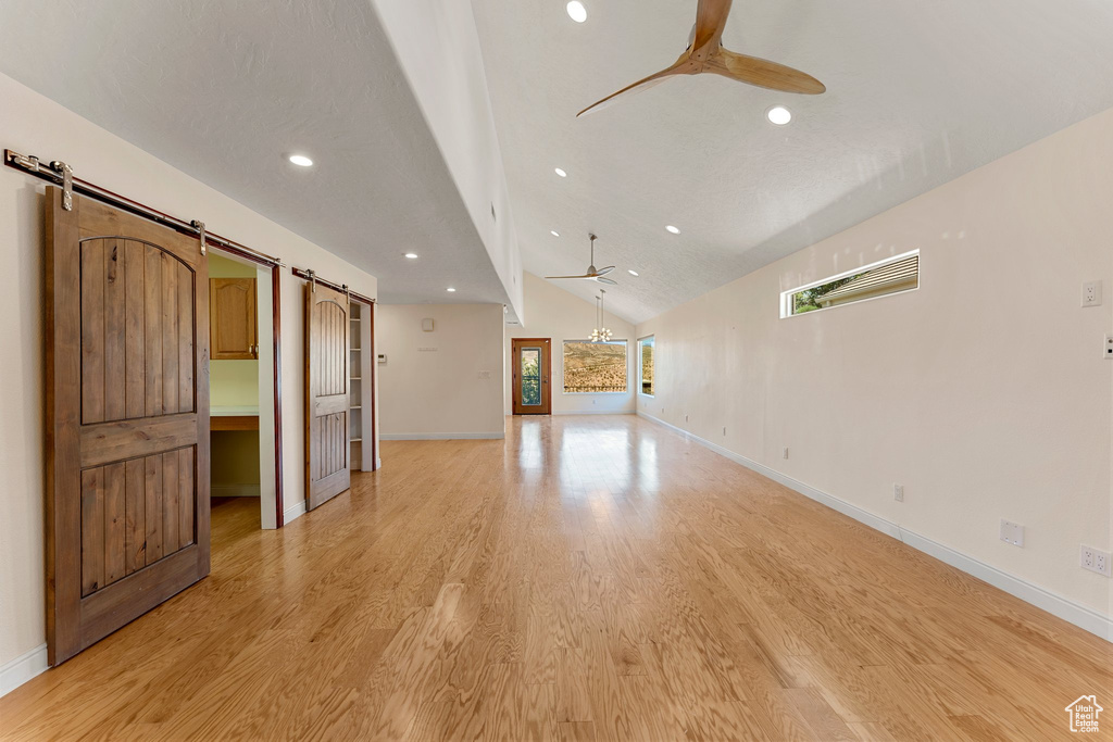 Unfurnished living room featuring a barn door, ceiling fan, light wood-type flooring, baseboards, and recessed lighting