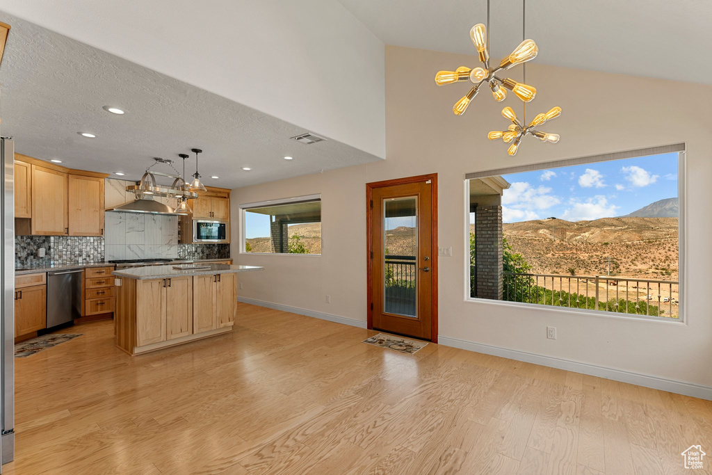 Kitchen with appliances with stainless steel finishes, a chandelier, light brown cabinets, light wood-style floors, and tasteful backsplash