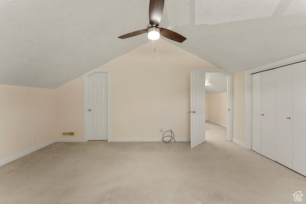 Bonus room featuring a textured ceiling, light colored carpet, vaulted ceiling, a ceiling fan, and baseboards