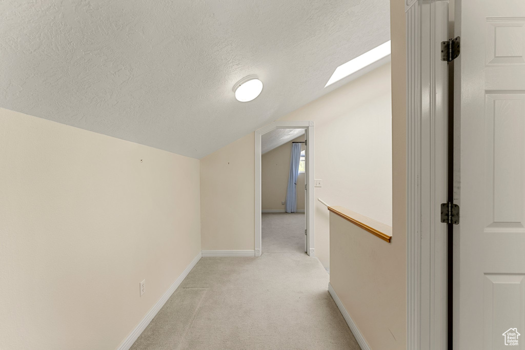 Hall with vaulted ceiling, light colored carpet, a textured ceiling, baseboards, and a skylight