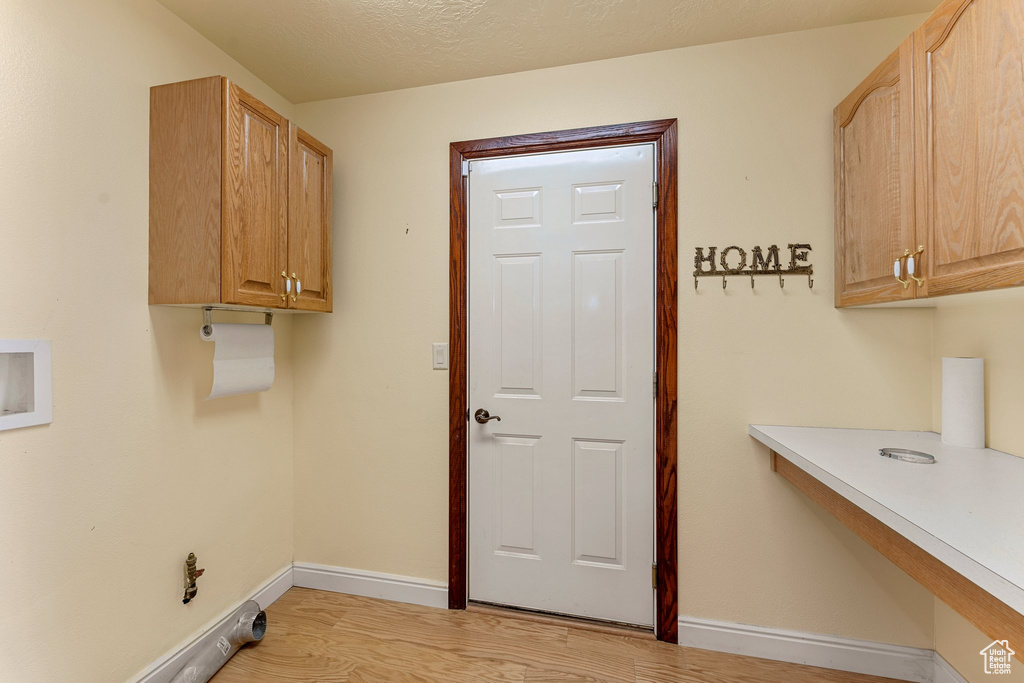 Washroom with cabinet space, light wood-style flooring, baseboards, and washer hookup