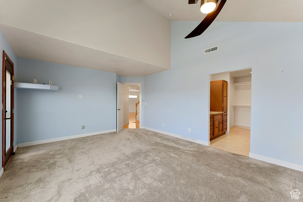 Unfurnished bedroom with light colored carpet, baseboards, high vaulted ceiling, and a ceiling fan