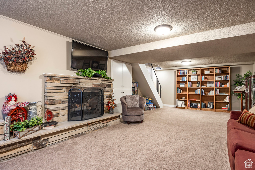 Living area featuring carpet floors, crown molding, a stone fireplace, stairway, and a textured ceiling