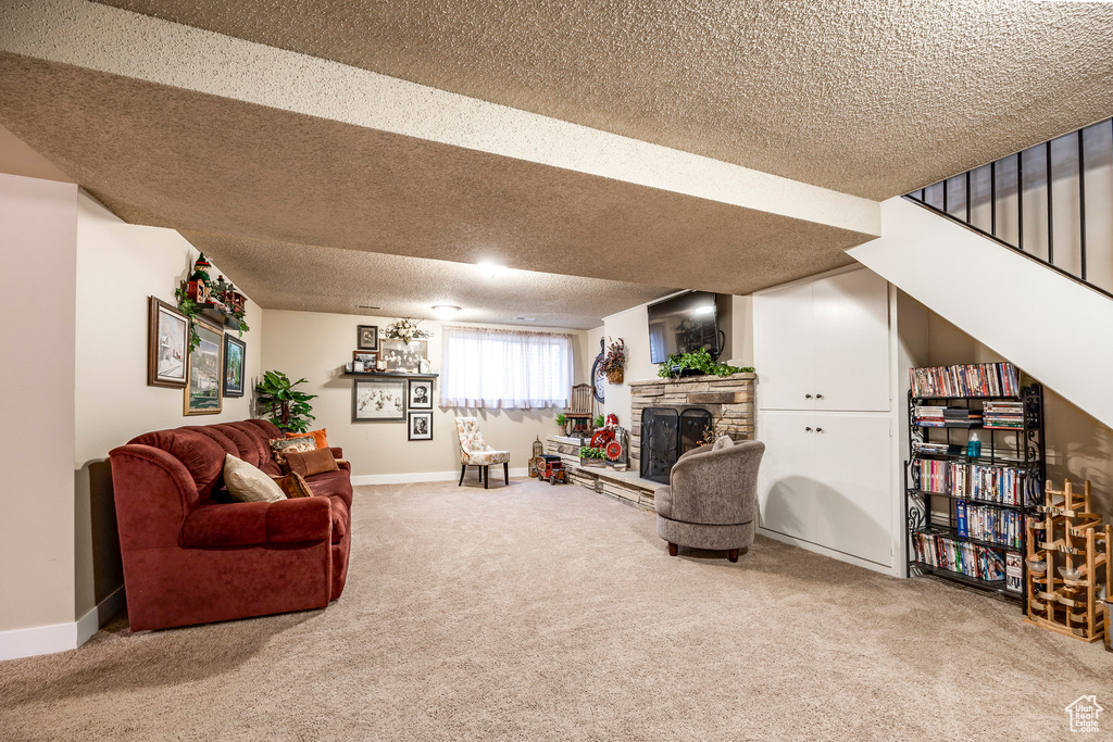 Carpeted living area with a stone fireplace, a textured ceiling, and baseboards