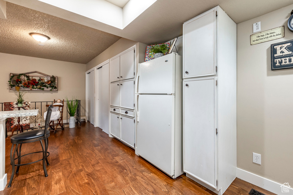 Kitchen featuring freestanding refrigerator, wood finished floors, baseboards, a textured ceiling, and white cabinets