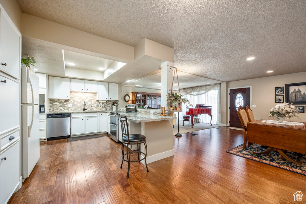 Kitchen with dark wood-style flooring, a peninsula, a sink, and appliances with stainless steel finishes