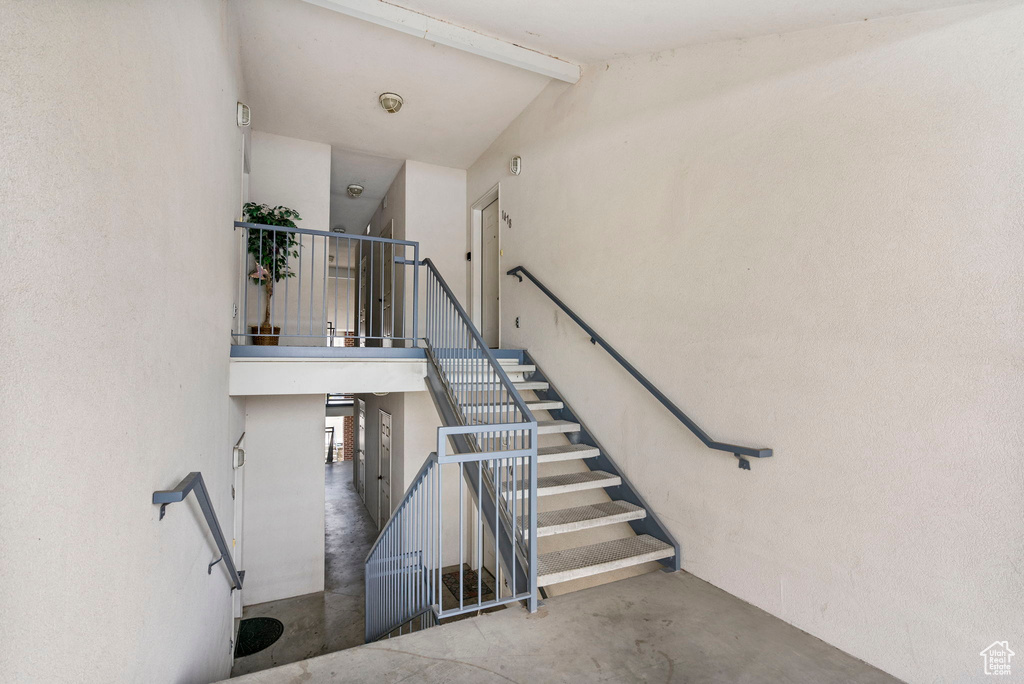 Staircase featuring beamed ceiling, high vaulted ceiling, and concrete floors