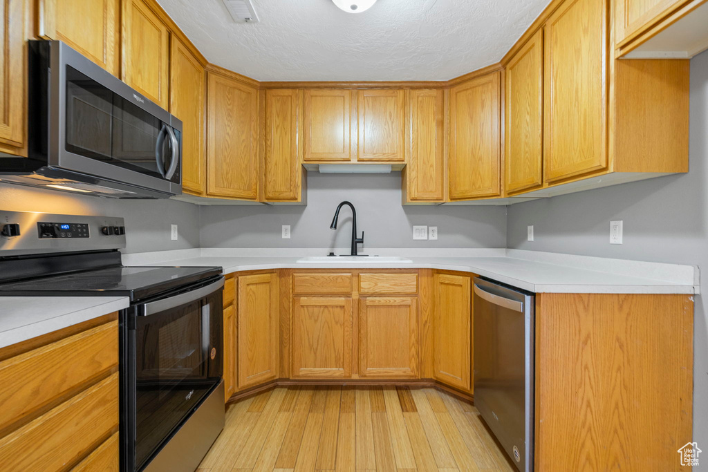 Kitchen with a textured ceiling, light hardwood / wood-style floors, sink, and appliances with stainless steel finishes