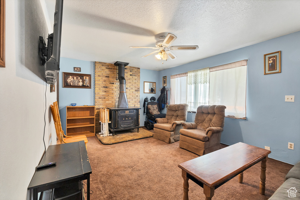 Carpeted living room with a wood stove, ceiling fan, and a textured ceiling