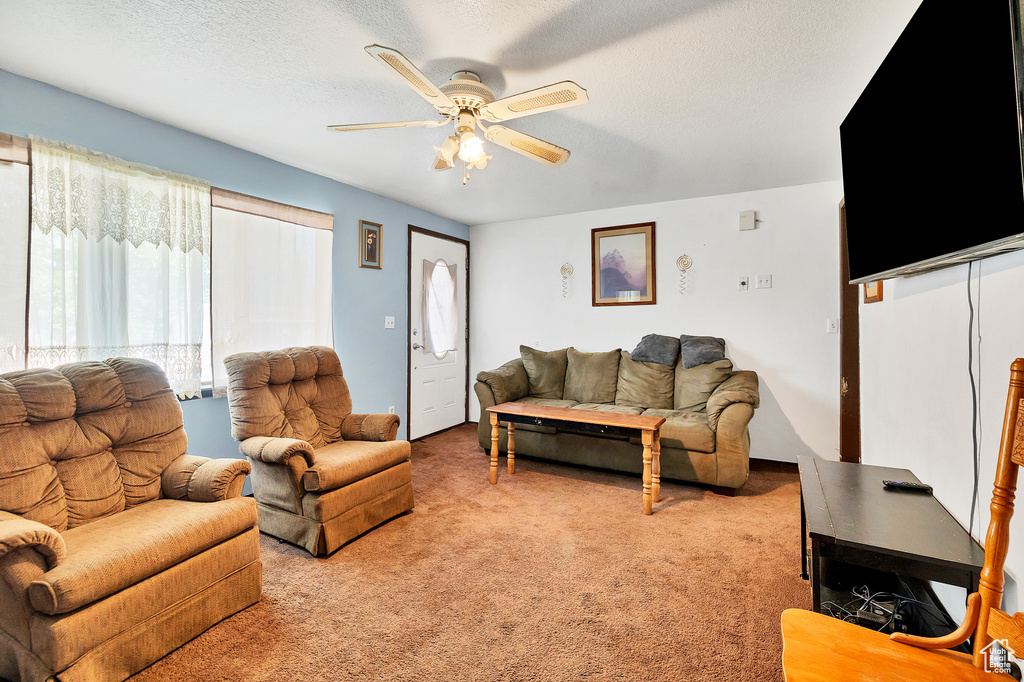 Living room with a textured ceiling, light colored carpet, and ceiling fan