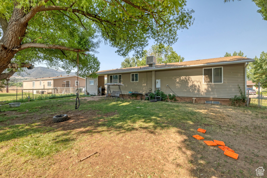 Back of house with central air condition unit and a yard