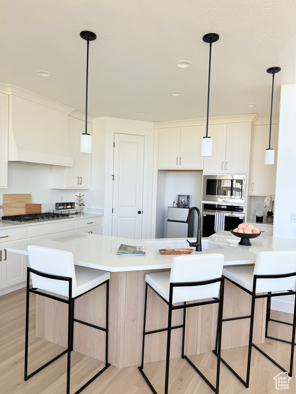 Kitchen with appliances with stainless steel finishes, light wood-type flooring, light countertops, white cabinetry, and recessed lighting