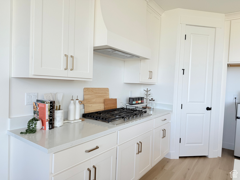 Kitchen with premium range hood, stainless steel gas stovetop, light wood-type flooring, white cabinets, and light countertops