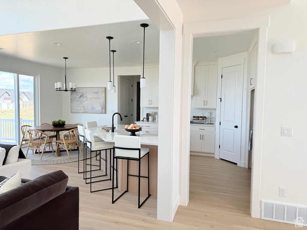 Kitchen with light wood-style flooring, a breakfast bar, white cabinetry, light countertops, and recessed lighting