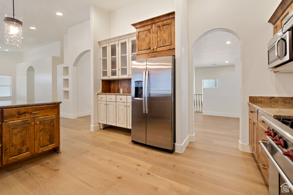 Kitchen featuring light stone countertops, stainless steel appliances, decorative light fixtures, and light wood-type flooring